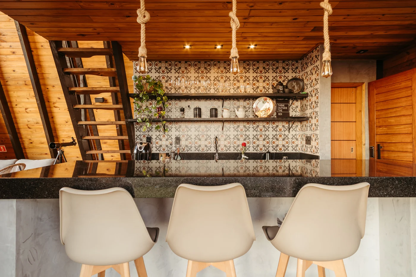 Kitchen breakfast bar with three white stools, patterned tiles and glassware shelves